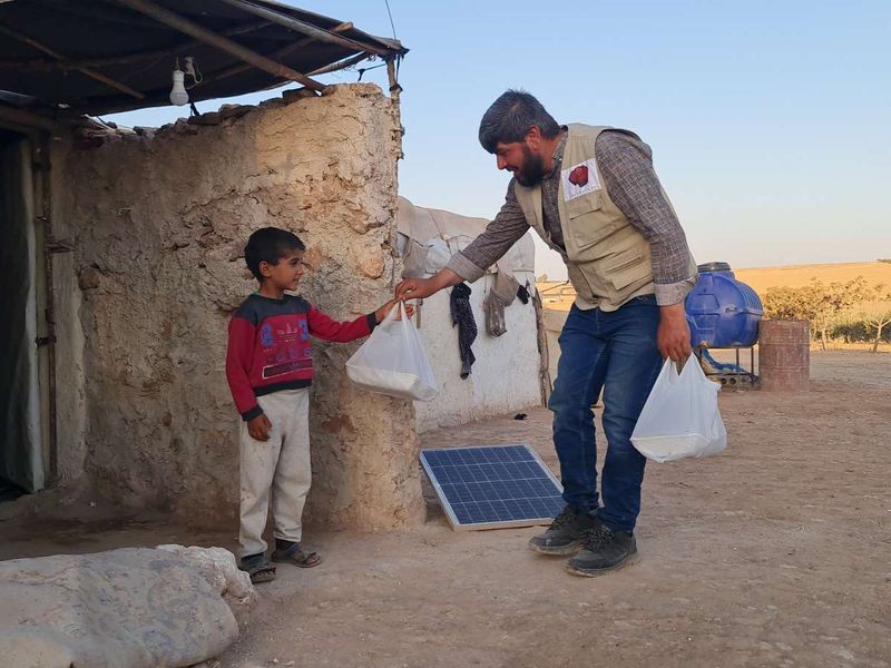 An aid worker handing food bags to a boy in Syria
