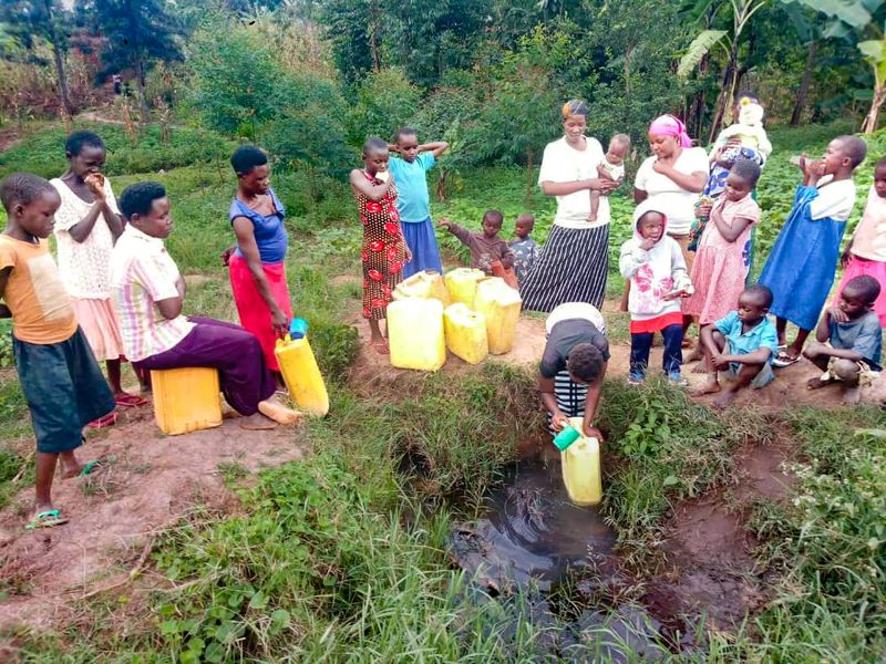 Women drawing water from an open pool in Uganda before a well was built
