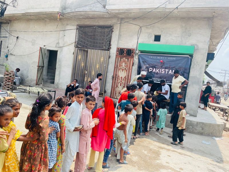 A queue for Rumi's Table meals in Pakistan under a Love Mercy Hope banner