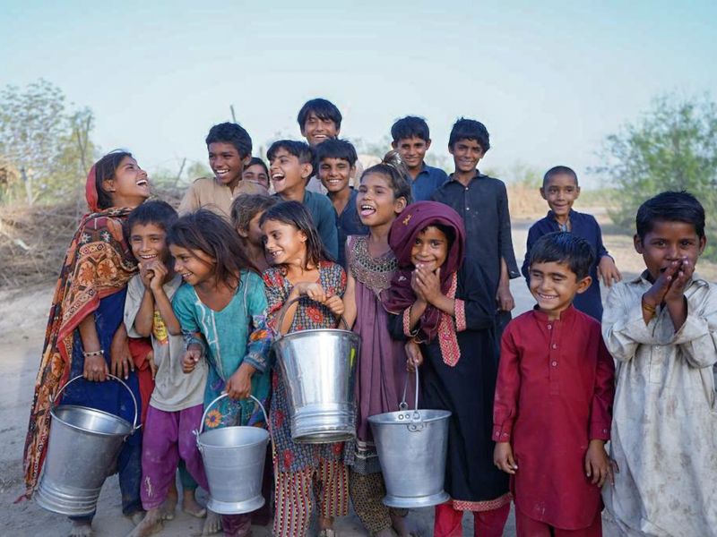 Children laughing as they carry buckets of clean water in Pakistan