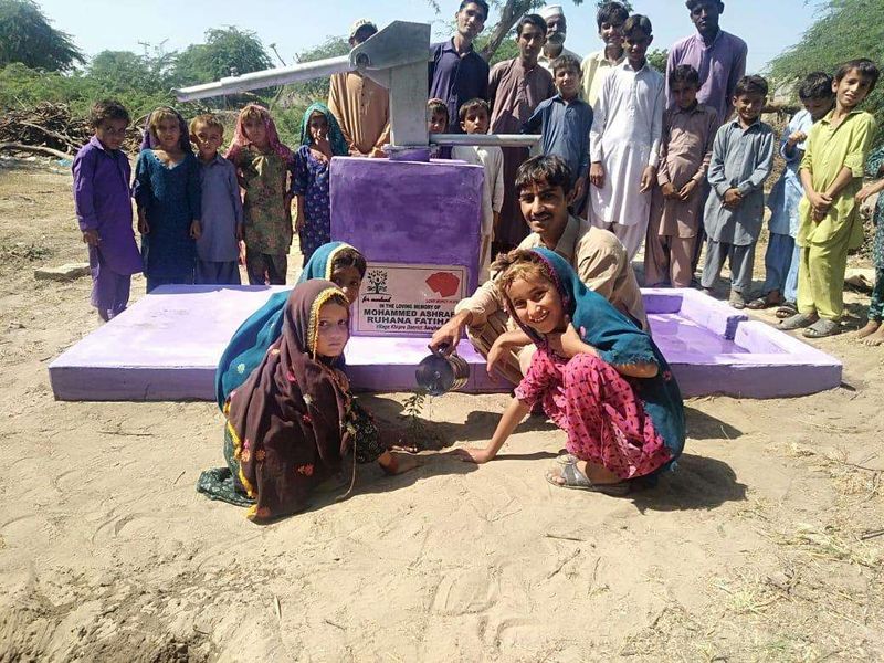 A community gathered at a large hand pump with a memorial plaque